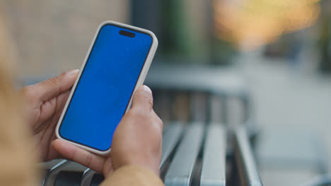 Close-Up-Of-Muslim-Man-Sitting-Outdoors-On-City-Street-Looking-At-Blue-Screen-Mobile-Phone